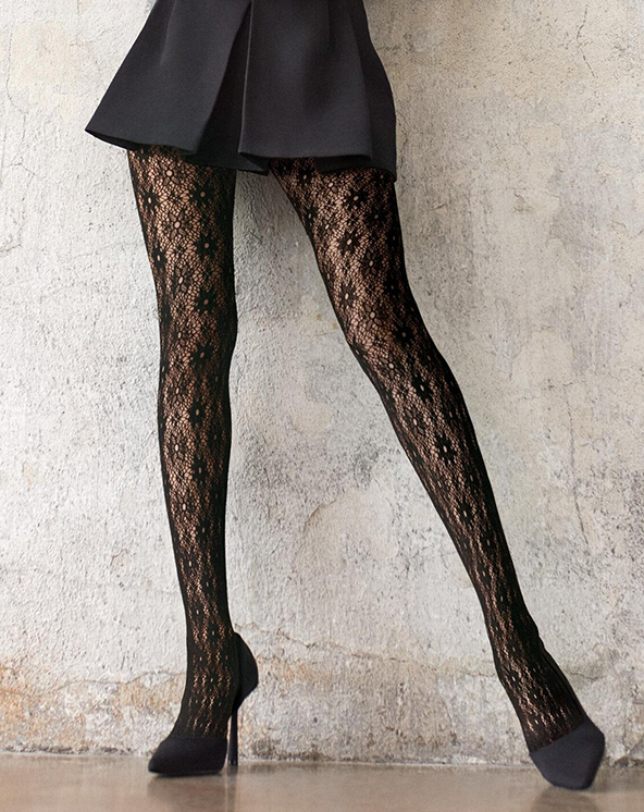 Crne čipkaste unihop čarape sa cvetićima koje osoba nosi uz teksturirani zid.