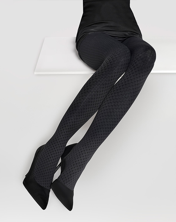 Osoba koja nosi crne šarene grilon unihop čarape na beloj pozadini sa crnim visokim potpeticama.