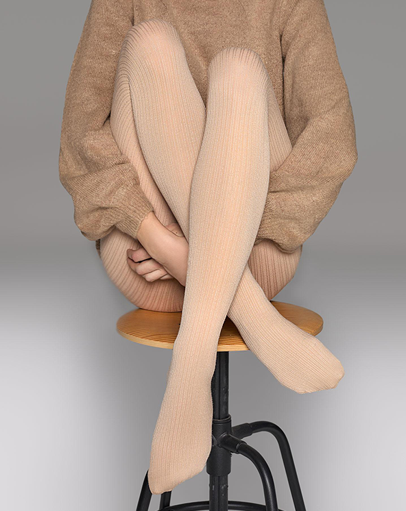 Devojka koja nosi bež unihop čarape od kašmira i sedi na stolici iza bele površine.