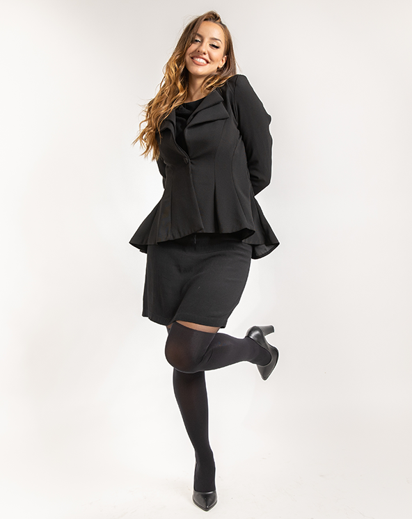 Devojka u crnoj peplum jakni sa jednom podignutom nogom u unihopu sa imitacijom čizmica i crnoj suknji na beloj pozadini.