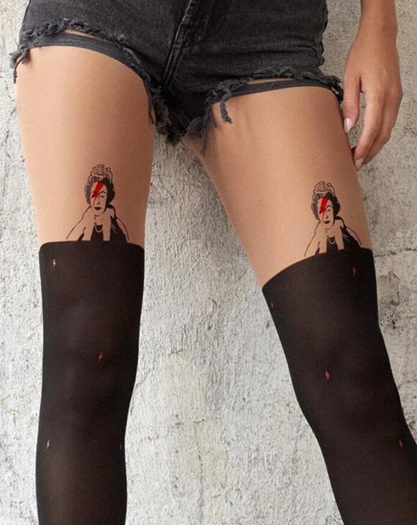 Model koja nosi crne čarape do butina sa dizajnom sličnim tetovažama na teksturiranoj pozadini zida.
